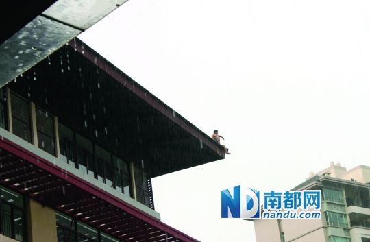 昨日上午，惠州市第一小学白鹭湖分校，讨薪男子冒雨坐在5楼楼顶。南都记者 陈伟斌 摄